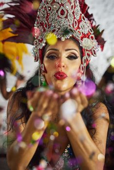 Making the night come alive. Shot of a samba dancer blowing confetti from her hands while performing in a carnival.
