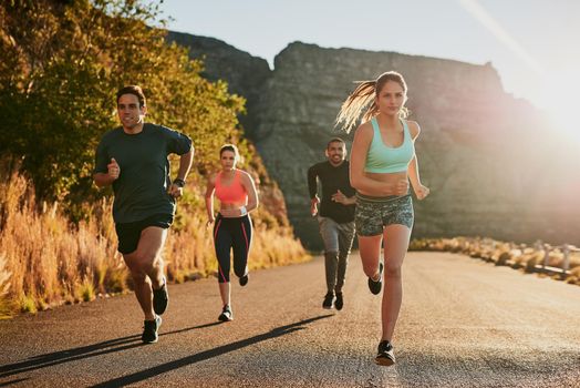 Add some spice to your workout routine. Shot of a fitness group running along a rural highway.