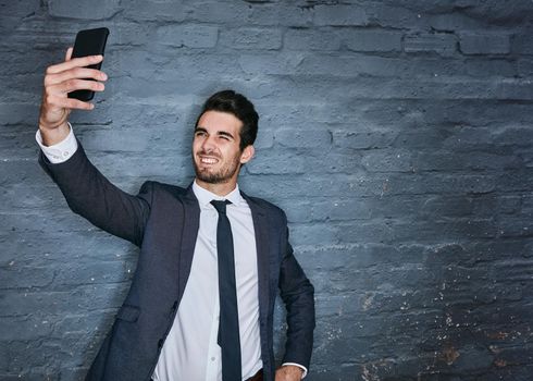 Taking a classy selfie. Shot of a businessman taking a selfie against a grey wall.