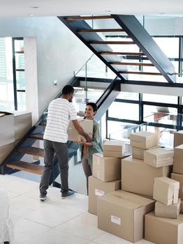 They make moving house look easy. Shot of a happy young couple passing boxes to each other while moving into their new home.