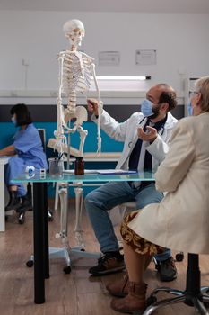 Physician showing human skeleton to pensioner woman