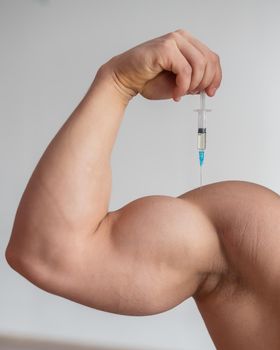 Closeup of a male hand with a dope syringe. Cropped biceps of a man. Unrecognizable bodybuilder sets himself growth hormone testosterone.