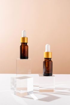 Amber glass dropper bottles with a pippette with white rubber tip on glass podium and beige background, mockup design