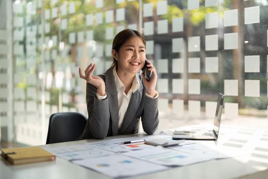 Smiling business asian woman in talking consultant on mobile phone at modern office