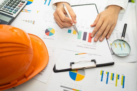 Engineer working project accounting with graph and construction helmet in office, Construction account concept.