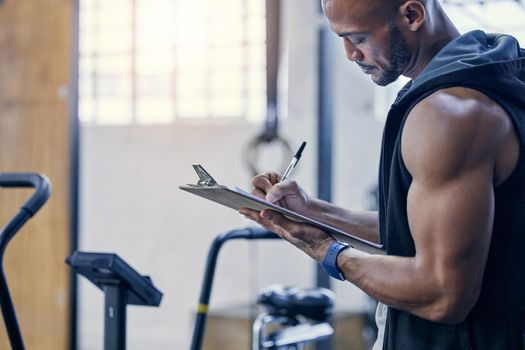 Organising and stocking supplies for all gym patrons. Shot of a muscular young man writing notes on a clipboard while working in a gym.