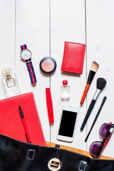 Cosmetics and women's accessories fell out of the black handbag on white background.