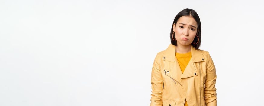 Portrait of sad korean woman sulking, frowning and looking upset, distressed frustrated face expression, standing gloomy against white background