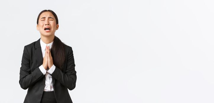 Overworked and distressed asian businesswoman begging for help, screaming hold hands together, pleading and crying desperate, standing upset over white background
