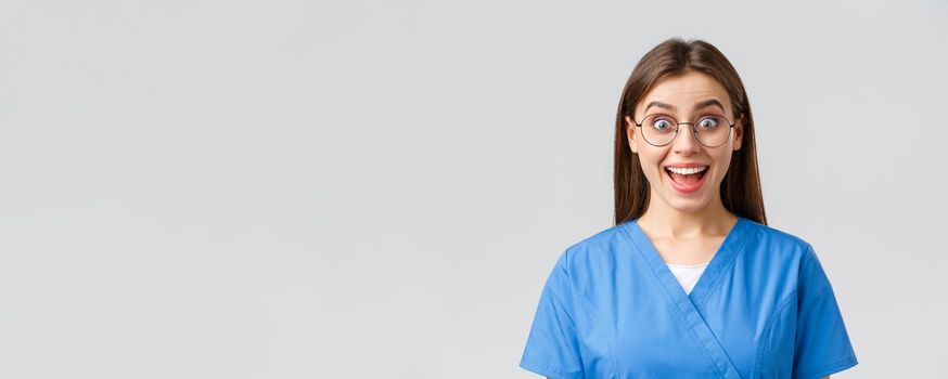 Healthcare workers, medicine, insurance and covid-19 pandemic concept. Enthusiastic upbeat female nurse, doctor in blue scrubs and glasses hear fantastic news, smiling amused