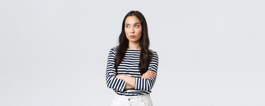 Lifestyle, beauty and fashion, people emotions concept. Annoyed and uninterested asian woman roll eyes, looking away bothered and bored, cross arms chest, standing white background.