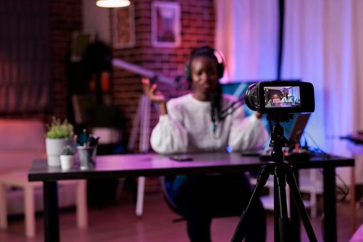 Young lifestyle vlogger filming online podcast show, talking to channel audience on camera. Female influencer recording live video online to create social media content, rpg lights studio.