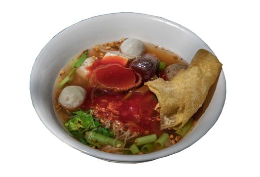 Traditional yentafo or Egg noodles soup with pink sauce and fish balls, shrimp ball, pork blood, chinese morning glory and fried wonton in white bowl.