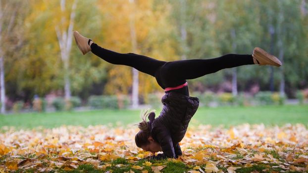 Girl performing gymnast stand on hands in autumn park