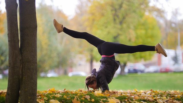 Girl performing gymnast stand on hands. Park, autumn