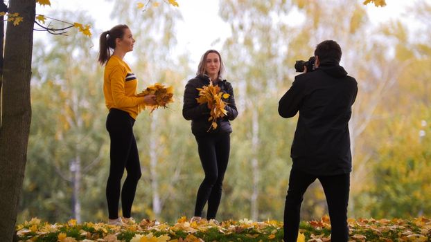Acrobatic girls posing in front of the photographer, holding yellow leaves.