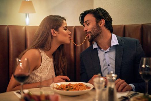 Shot of a young couple sharing spaghetti during a romantic dinner at a restaurant.