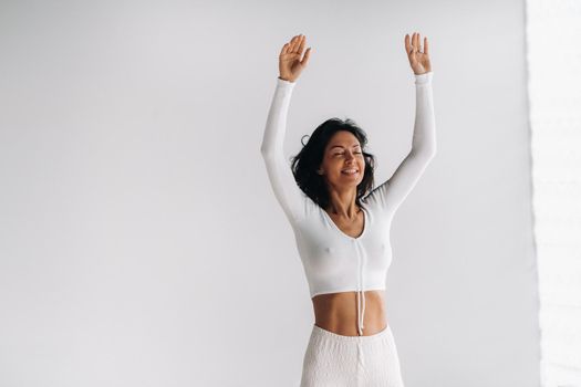 a female yogi in white clothes with her hands up meditates in the Yoga hall.