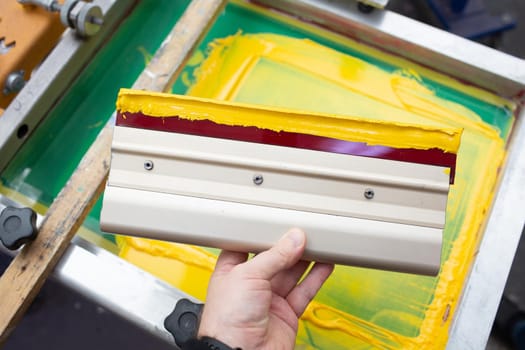 Squeegee for Serigraphy silk screen print process at clothes factory. Frame, squeegee and plastisol color paints