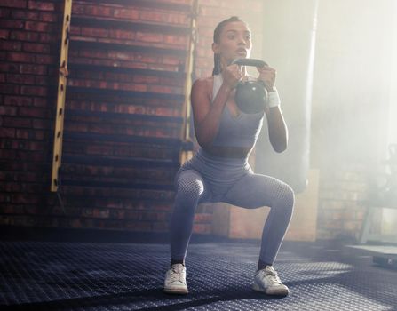 Burn fat and build strength with every squat. Shot of a sporty young woman doing kettlebell squats in a gym.