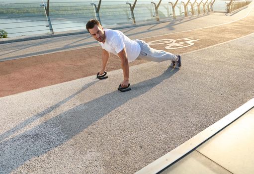 Full length portrait of a handsome middle aged European man, muscular build athlete doing push ups during an outdoor workout on the city bridge early in the morning