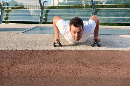 Front view of a determined sportsman doing push-ups , pumping chest and shoulders muscles during morning workout outdoor. Keep your body fit and enjoy summer moments