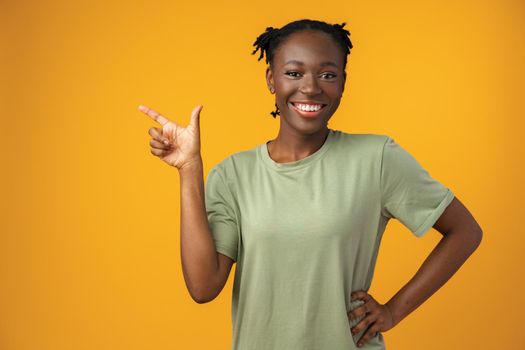 Cheerful Afro woman points to copy space in yellow studio
