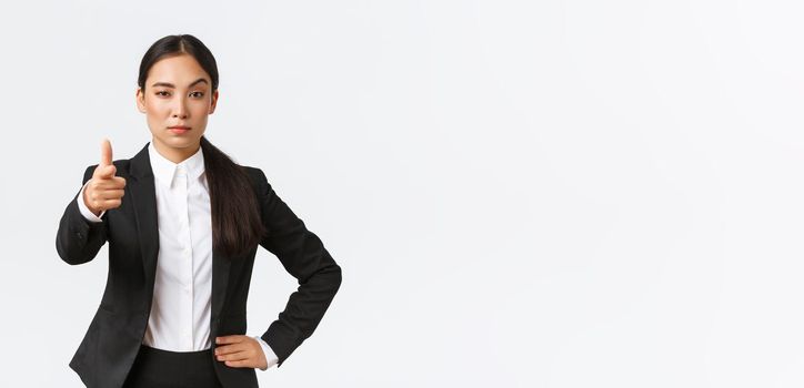 Confident strict office manager, asian female entrepreneur pointing finger at camera and looking serious, propose job offer, give task, picking employee for work, standing white background