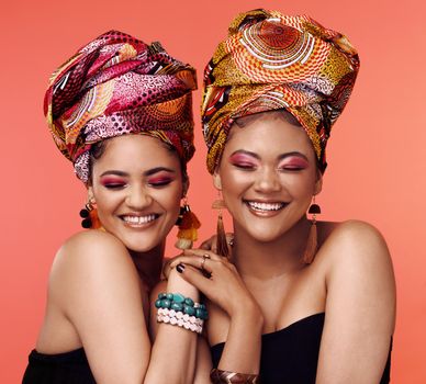 My sister is my best friend. Studio shot of two attractive young women wearing traditional African head wraps posing together against an orange background.