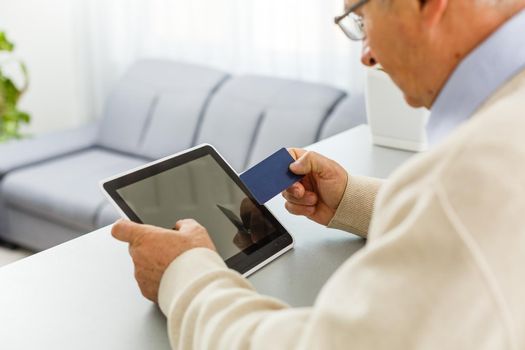 Senior man at laptop paying with credit card for online shopping