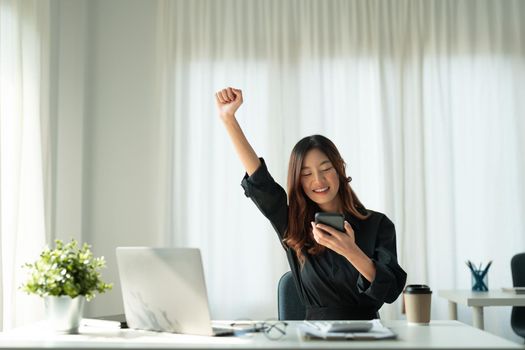 Portrait of happy young business asian woman celebrating success with arms up in front of laptop computer.positive expression, sucess in business concept.