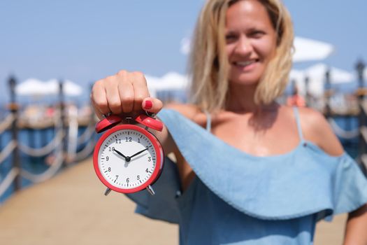 Smiling female tourist holding an alarm clock on sea pier