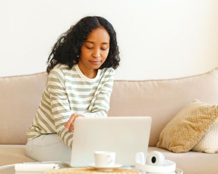 African-American female sitting on sofa and using digital device for work and study