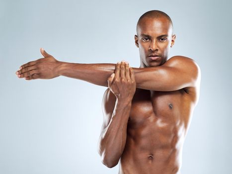 Dedication will get you far. Studio shot of an athletic young man doing stretching exercises while posing against a grey background.