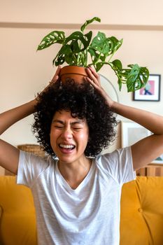 Young playful African American woman having fun, being carefree putting potted plant on her head. Vertical image.