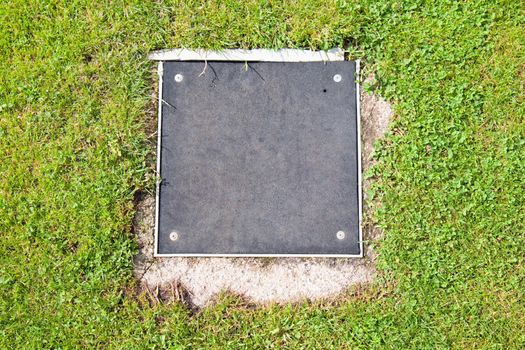 Metal manhole cover drainage system in the midst of cropped grass