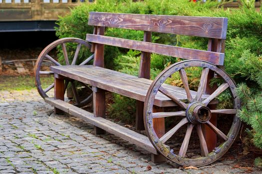 Wooden vintage bench with cart wheels on paving stones