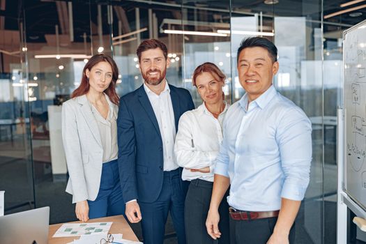Happy diverse professional business team stand in office near each other looking at camera, smiling