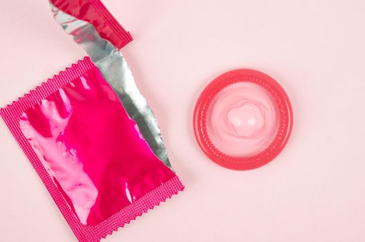 Pink opened condom and condom in pack on a pink background.