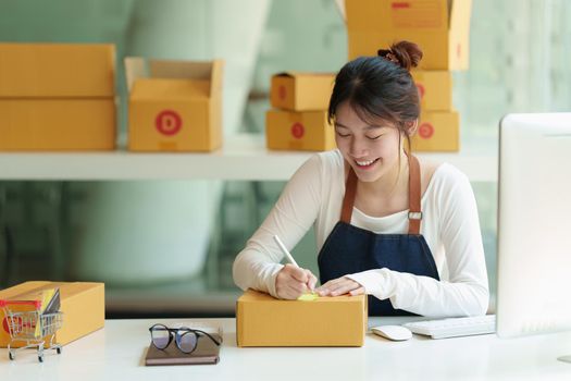 Asian small business owner with packing parcel box at home office, SME e commerce concept.