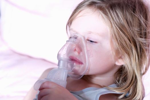 Sick little girl in medical oxygen mask using nebulizer