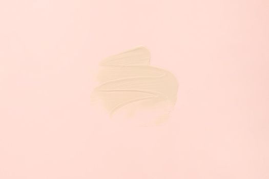 Sample texture of foundation cream for the face close-up. A smear of foundation on a pastel pink background.