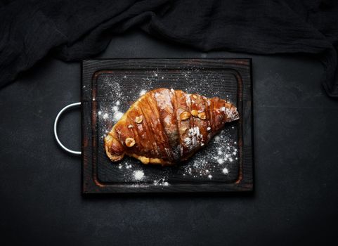 Baked croissants on a black wooden board sprinkled with powdered sugar