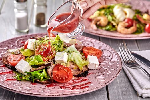 Healthy mixed Greek salad served on a pink plate with silver fork containing crisp leafy greens, microgreen, feta, onion, tomato and sliced beef