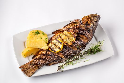 Grilled carp fish with rosemary potatoes and lemon, close up