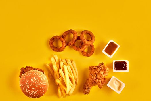 Fast food dish top view. French fries, hamburger, mayonnaise and ketchup sauces on yellow background.