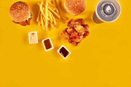 Fast food dish top view. French fries, hamburger, mayonnaise and ketchup sauces on yellow background.