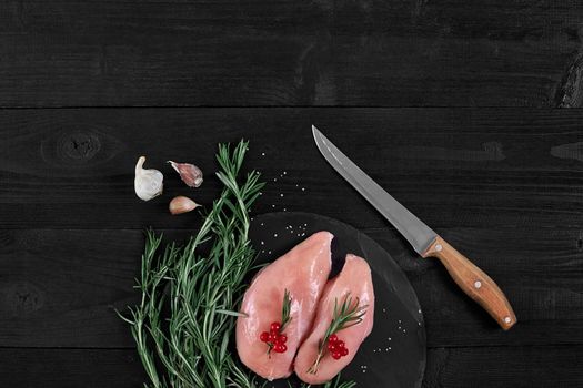 Chicken breast on a cutting board with herbs, spices and knife on rustic wooden background.