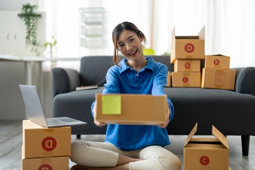 Young Asian Woman holding parcel box for delivery to customer by logistic service. small business entrepreneur SME distribution warehouse. small owner home office and Online marketing product theme