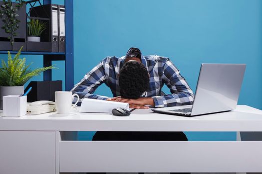 Exhausted and tired young adult office worker falling asleep on desk because of overtime work hours.